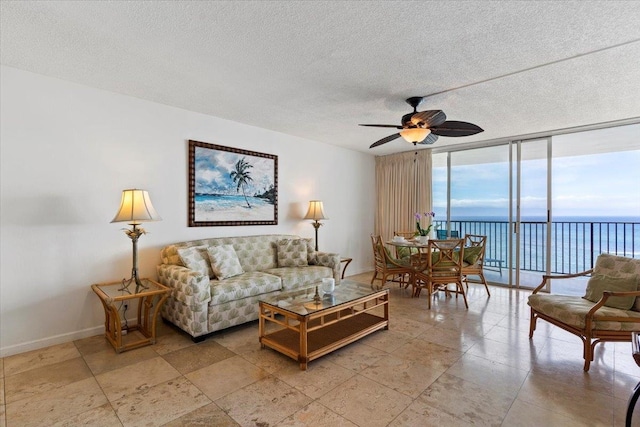 living room with a textured ceiling, expansive windows, a water view, and ceiling fan