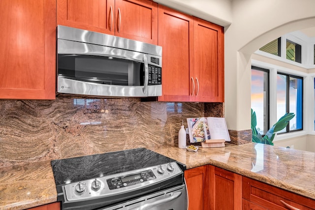 kitchen featuring backsplash, arched walkways, light stone countertops, and appliances with stainless steel finishes