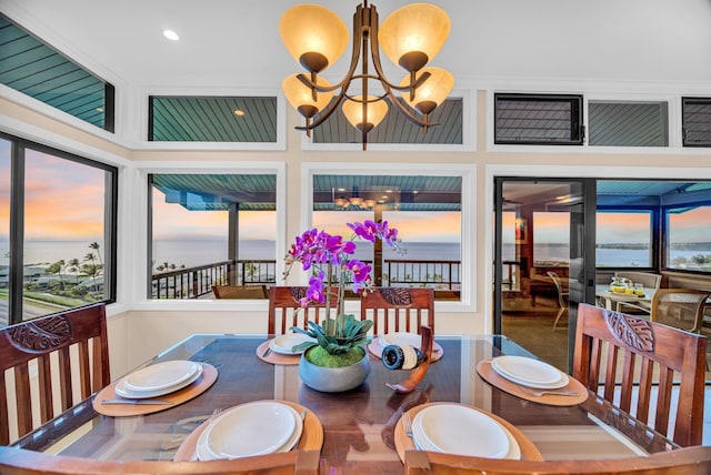 dining space with a water view, recessed lighting, a towering ceiling, and a notable chandelier