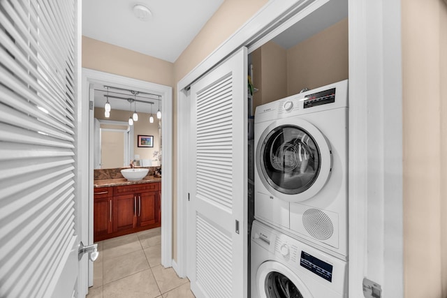 washroom with light tile patterned flooring, laundry area, a sink, and stacked washer / dryer
