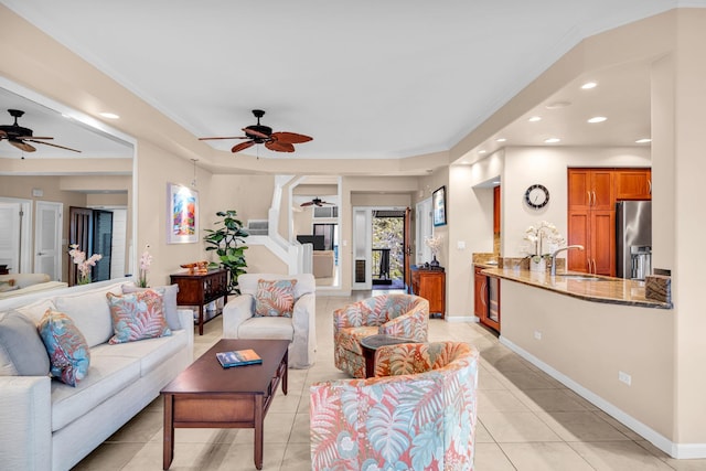 living room featuring light tile patterned floors, baseboards, ornamental molding, and a ceiling fan