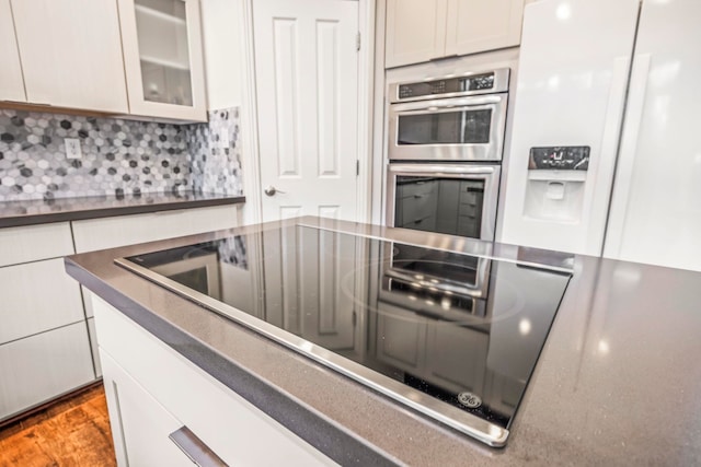 kitchen with decorative backsplash, stainless steel double oven, white cabinetry, and white fridge with ice dispenser