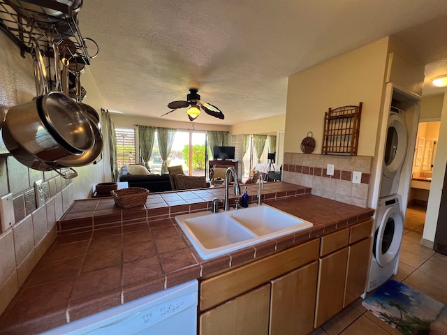 kitchen with sink, stacked washer / dryer, tile counters, and white dishwasher