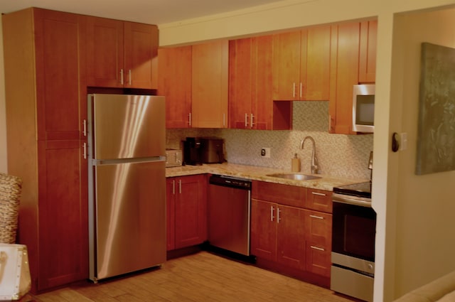 kitchen featuring backsplash, light hardwood / wood-style floors, stainless steel appliances, sink, and light stone counters