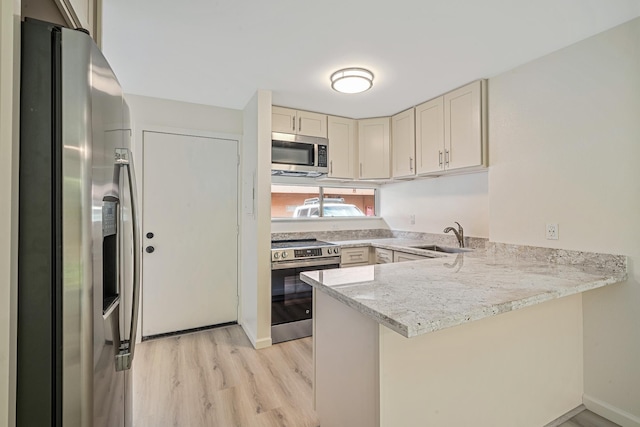 kitchen with light wood finished floors, a peninsula, stainless steel appliances, cream cabinetry, and a sink