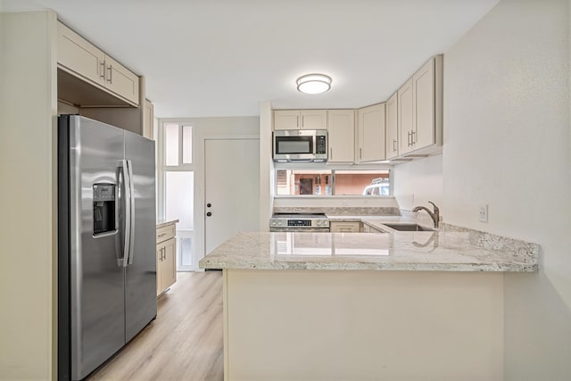 kitchen with stainless steel appliances, a sink, a peninsula, and cream cabinets