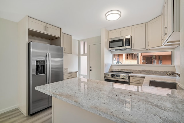 kitchen with light stone counters, stainless steel appliances, a sink, light wood-type flooring, and a peninsula