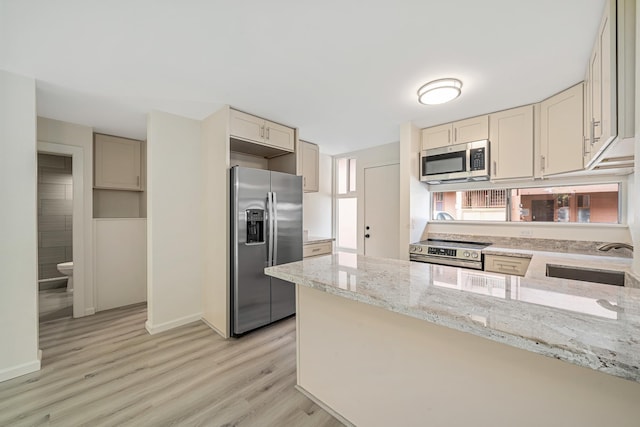 kitchen with appliances with stainless steel finishes, a peninsula, light stone countertops, light wood-style floors, and a sink