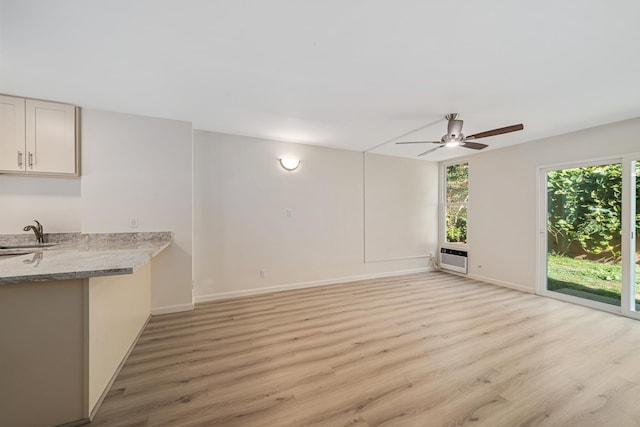 unfurnished living room with baseboards, ceiling fan, an AC wall unit, light wood-type flooring, and a sink