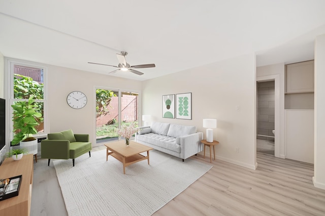 living room with light wood-type flooring, baseboards, and a ceiling fan