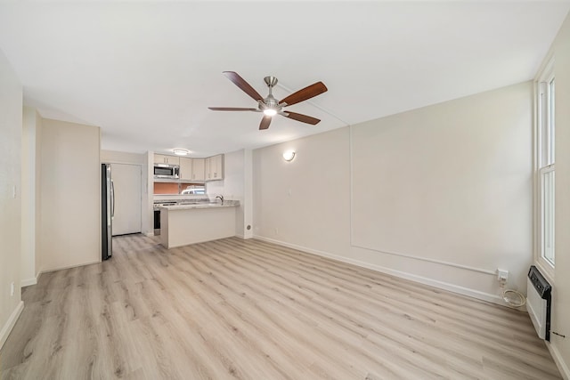 unfurnished living room featuring ceiling fan, light wood-style flooring, and baseboards