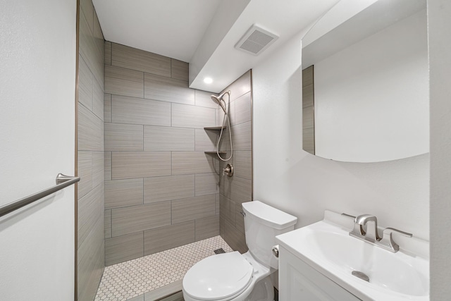 full bathroom featuring toilet, visible vents, tiled shower, and vanity