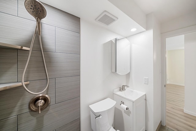 full bathroom with visible vents, a tile shower, vanity, and toilet