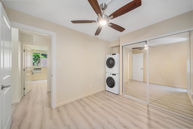 laundry area with light wood-type flooring, stacked washer and clothes dryer, baseboards, and laundry area