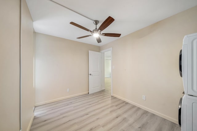 unfurnished bedroom featuring stacked washing maching and dryer, baseboards, light wood finished floors, and a ceiling fan