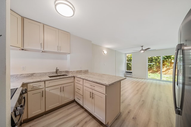 kitchen with light stone counters, a peninsula, stainless steel appliances, light wood-style floors, and a sink