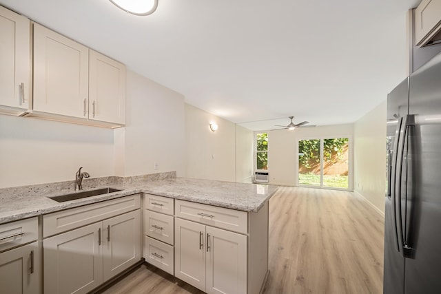 kitchen with stainless steel fridge, light stone counters, a peninsula, light wood-style floors, and a sink