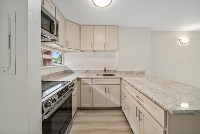 kitchen with light stone counters, stainless steel appliances, a peninsula, a sink, and light wood-type flooring