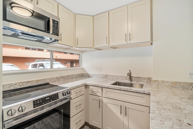 kitchen featuring stainless steel appliances, a sink, cream cabinets, and light stone countertops