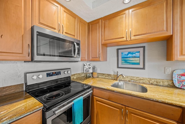 kitchen with stainless steel appliances, brown cabinets, a sink, and light stone countertops