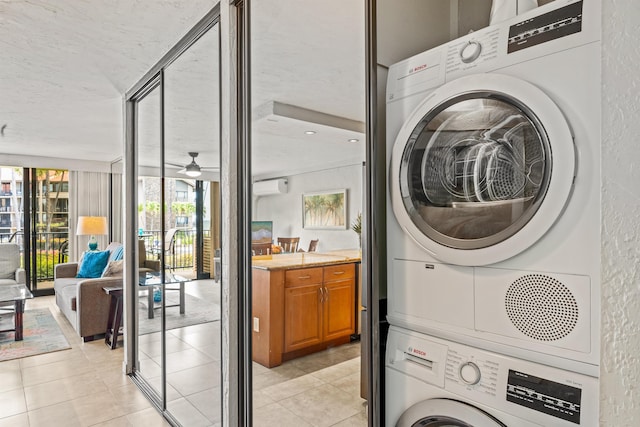 clothes washing area with stacked washer and clothes dryer, a wall unit AC, light tile patterned floors, ceiling fan, and a textured ceiling