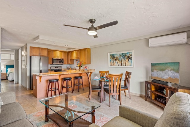 living room featuring light tile patterned floors, a textured ceiling, a ceiling fan, baseboards, and an AC wall unit