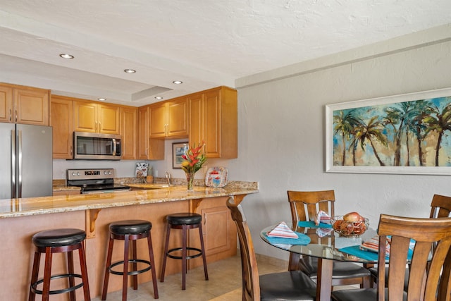 kitchen featuring a breakfast bar area, appliances with stainless steel finishes, light stone counters, and recessed lighting