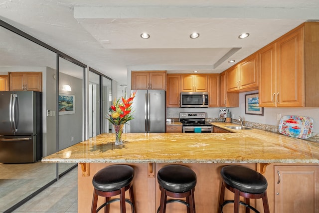 kitchen featuring appliances with stainless steel finishes, a sink, a peninsula, and light stone countertops