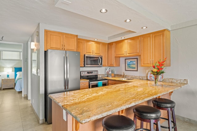 kitchen with light stone counters, a breakfast bar area, stainless steel appliances, a sink, and a peninsula