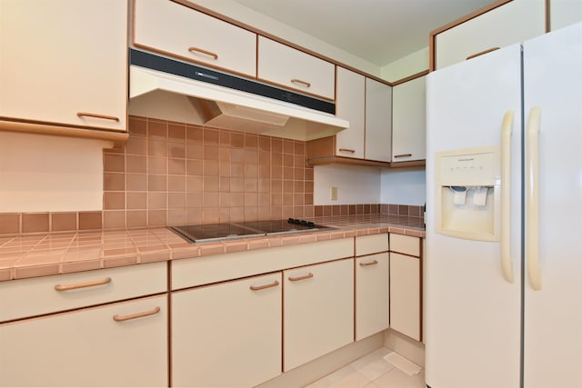 kitchen featuring tile counters, light tile patterned floors, decorative backsplash, and white fridge with ice dispenser