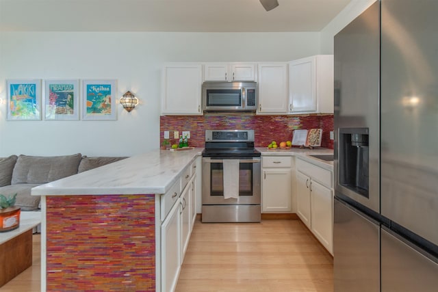 568 Hana Hwy Unit B, Paia, HI 96779 - kitchen featuring appliances with stainless steel finishes, a peninsula, light wood-style floors, backsplash, and white cabinets