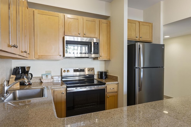 kitchen featuring light stone counters, appliances with stainless steel finishes, light brown cabinetry, and sink