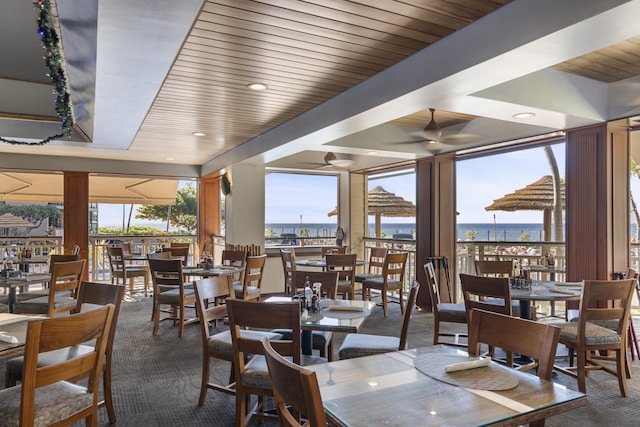 carpeted dining space featuring a water view, ceiling fan, plenty of natural light, and wooden ceiling