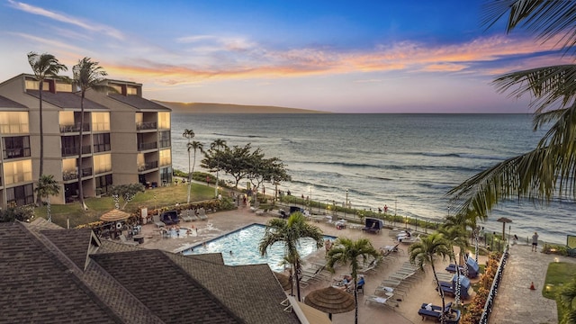 pool at dusk featuring a patio and a water view