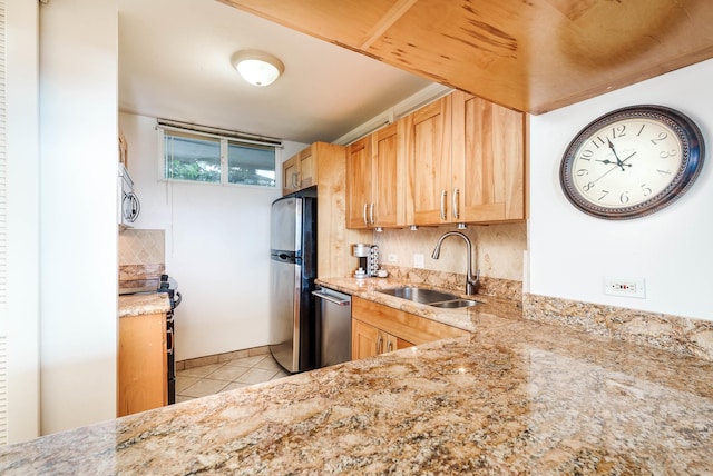 kitchen with appliances with stainless steel finishes, light stone countertops, a sink, and light tile patterned floors