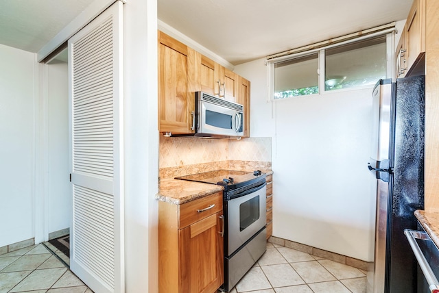 kitchen featuring appliances with stainless steel finishes, light tile patterned floors, light stone counters, and backsplash