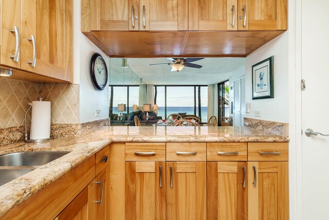 kitchen with light stone counters, kitchen peninsula, ceiling fan, and tasteful backsplash