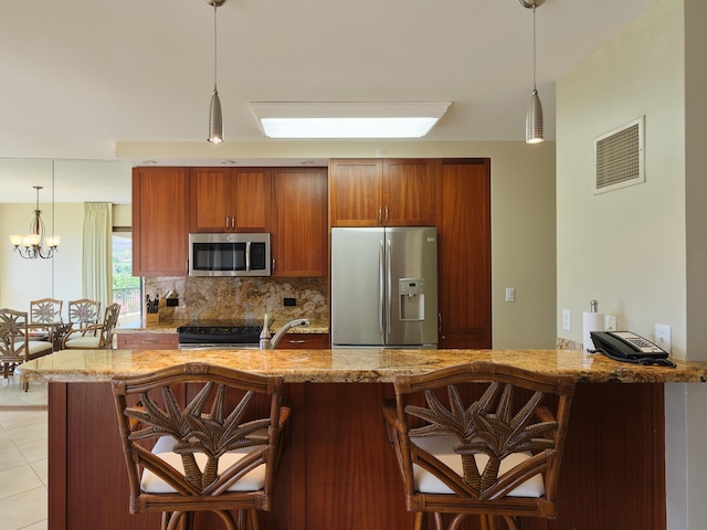 kitchen featuring stainless steel appliances, kitchen peninsula, a notable chandelier, a breakfast bar, and backsplash