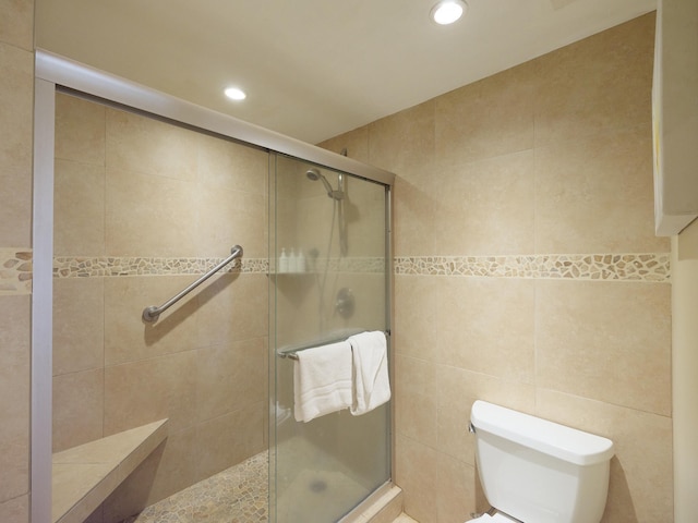 bathroom with tile walls, toilet, and a shower with shower door