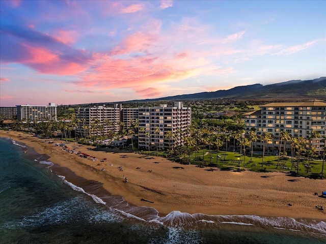 aerial view at dusk with a water and mountain view and a view of the beach