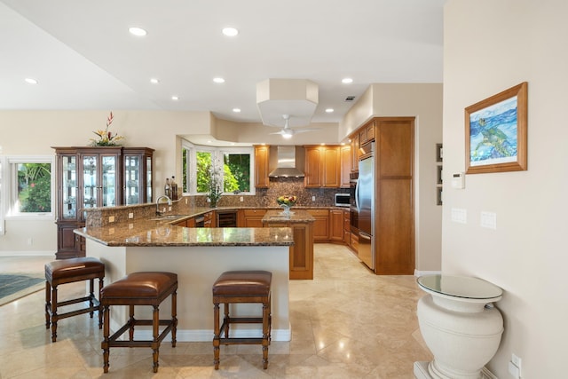 kitchen featuring kitchen peninsula, sink, a breakfast bar area, and wall chimney range hood