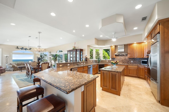 kitchen with ceiling fan with notable chandelier, wall chimney range hood, decorative light fixtures, a large island, and beverage cooler