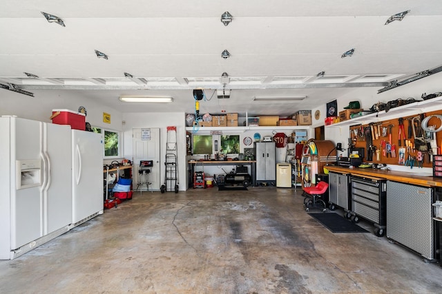 garage with a workshop area, white fridge, white refrigerator with ice dispenser, and a garage door opener