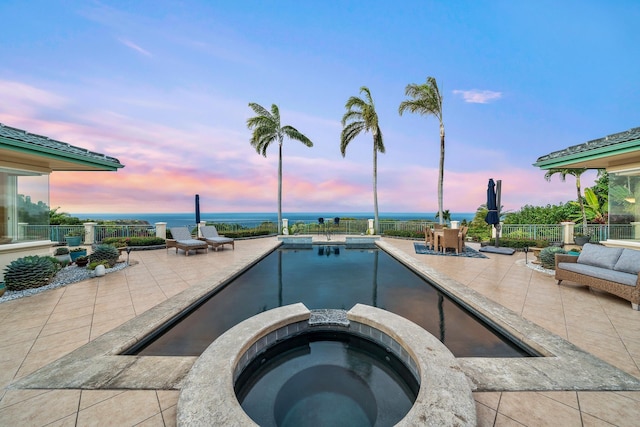 pool at dusk with a patio area and an in ground hot tub