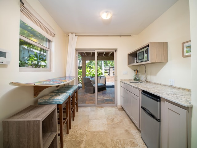 kitchen with stainless steel dishwasher, gray cabinetry, light stone counters, light tile patterned floors, and sink