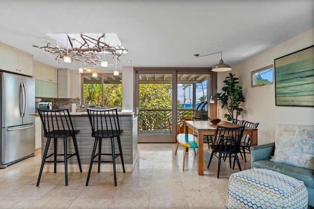 interior space featuring decorative backsplash, a chandelier, stainless steel refrigerator, light tile patterned floors, and decorative light fixtures