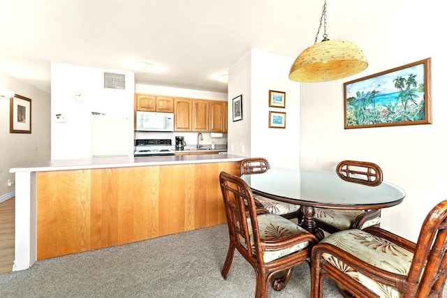 kitchen with pendant lighting, white appliances, light carpet, sink, and kitchen peninsula