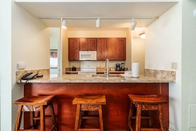 kitchen featuring sink, kitchen peninsula, white appliances, rail lighting, and a breakfast bar area