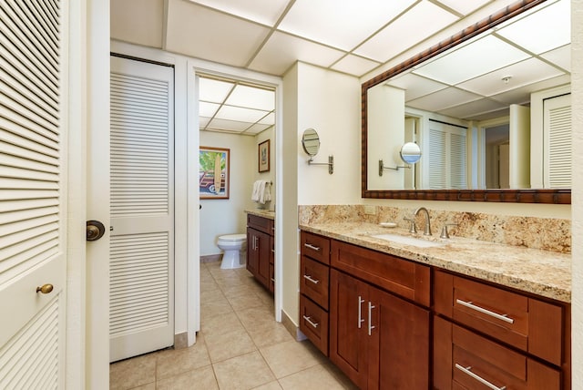 bathroom featuring vanity, a drop ceiling, toilet, and tile patterned floors