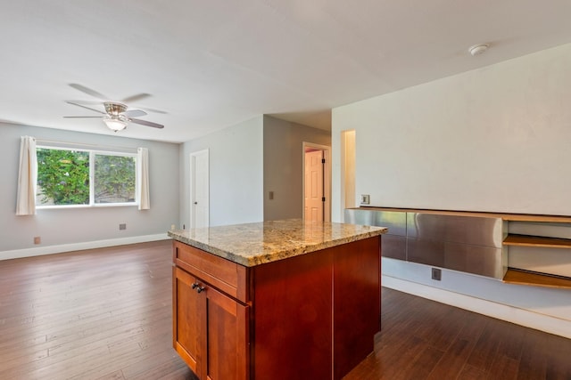 kitchen featuring light stone counters, a center island, dark wood finished floors, open floor plan, and baseboards